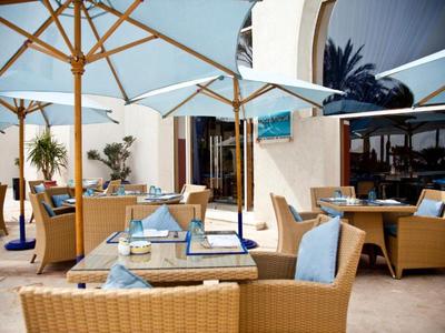 Einladende Hotelterrasse mit Korbsesseln, Tischen und Sonnenschirmen bei Tageslicht.