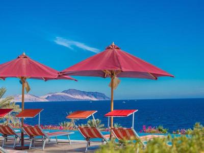 Rote Sonnenschirme und Liegestühle am Strand mit Blick auf das blaue Meer und den klaren Himmel.