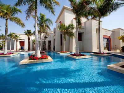 Ein luxuriöses Hotel mit einem großen Pool, umgeben von Palmen und weißen Gebäuden.