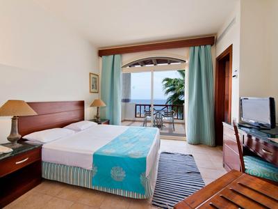 Hotelzimmer mit Doppelbett, Schreibtisch und Balkon mit Meerblick unter klarem Himmel.