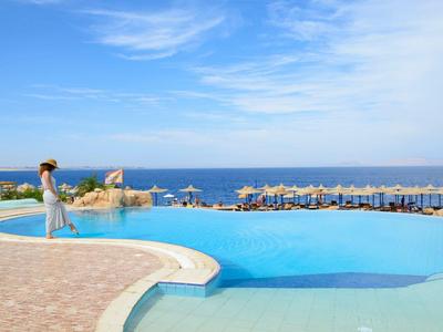 Frau steht am Rand eines Infinity-Pools mit Meerblick und blauem Himmel.