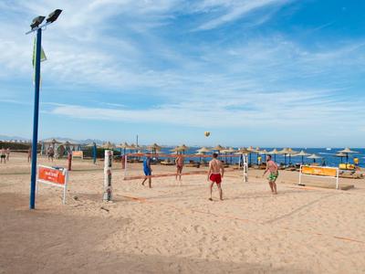 Menschen spielen Beachvolleyball am sonnigen Strand mit Blick auf das Meer und die Stadt.