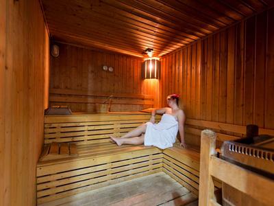 Frau entspannt auf Holzbänken in einer warm beleuchteten Sauna mit Holzverkleidung.