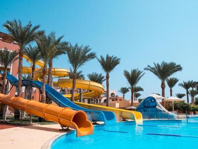 Parc aquatique avec toboggans colorés et palmiers sous un ciel bleu clair.