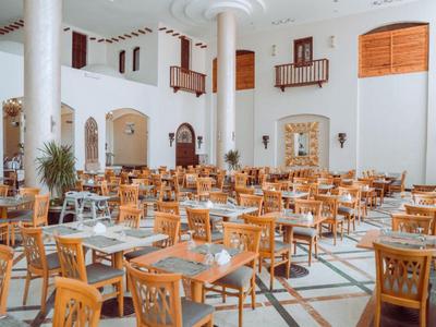 Salle à manger d'hôtel lumineuse et spacieuse avec tables en bois, chaises et grandes colonnes blanches.