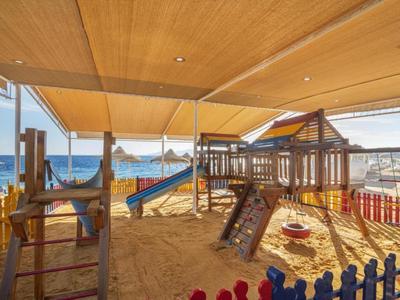 Kinderspielplatz mit Sand, Klettergerüst und Rutsche am Strand mit Blick auf das Meer