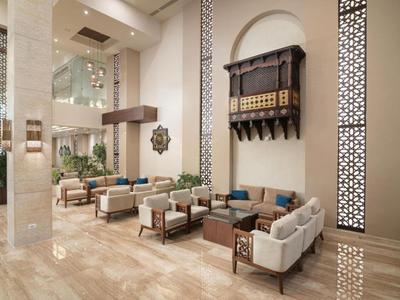 Elegante Hotellobby mit bequemen Sesseln, Couchtischen und dekorativen Wandornamenten in hellem Ambiente.