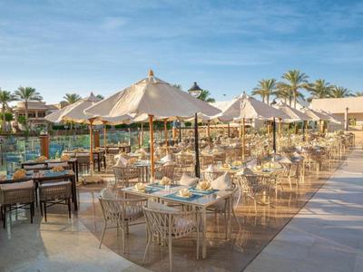 Restaurantterrasse mit weißen Sonnenschirmen und Stühlen neben einem Pool bei klarem Himmel.