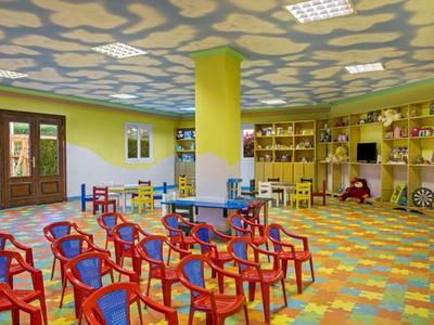 Bunter Kinderspielraum mit Stühlen, Tischen und Bücherregalen in einer Hotelumgebung.