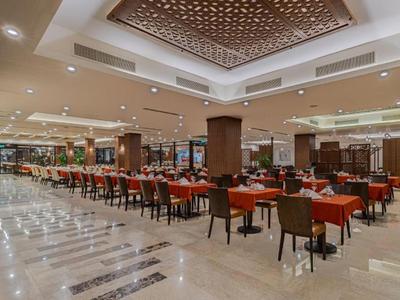 Großes Hotelrestaurant mit rot gedeckten Tischen und braunen Stühlen auf hellem Marmorboden.