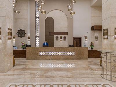 Moderner Hotellobby mit Marmorfußboden, Empfangstresen und dekorativen Leuchten in hellem Design.