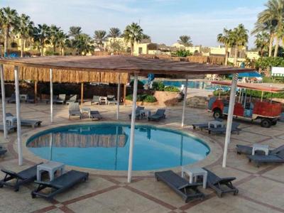 Poolbereich eines Hotels mit Sonnenschutz, Liegen und Palmen bei Tageslicht.