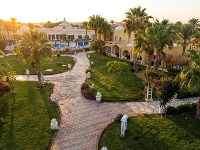 Sonniger Garten mit Wegen, Palmen und Gebäude im Hintergrund eines Resorts.