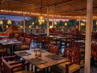 Offener Restaurantbereich mit Holztischen und Stühlen, beleuchtet bei Sonnenuntergang.