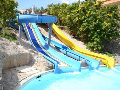 Drei Wasserrutschen führen in einen Pool, umgeben von Pflanzen und einem sonnigen Bereich.