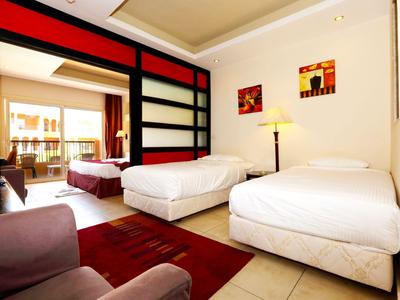 Helles Hotelzimmer mit zwei Einzelbetten, Teppich, Sessel und Zugang zu Balkon.