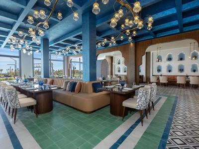 Nowoczesna restauracja hotelowa z niebieskimi belkami sufitowymi i dekoracyjnymi lampami wiszącymi.