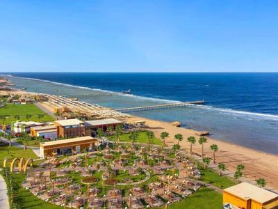 Obiekt hotelowy z basenem, leżakami, palmami i bezpośrednim dostępem do plaży pod błękitnym niebem.