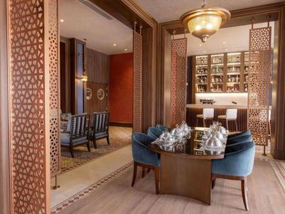 Elegancka strefa lounge w hotelu z niebieskimi fotelami, drewnianym stołem i dekoracyjnymi panelami drewnianymi