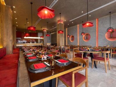 Nowoczesna restauracja z czerwonymi lampami wiszącymi i nakrytymi stołami w stylowej atmosferze.