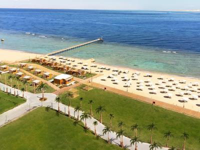 Hotel przy plaży z piaskiem, leżakami i parasolami przy czystym niebieskim morzu.
