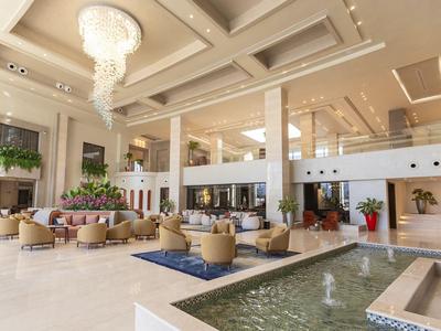 Przestronny hol hotelowy z żyrandolem, miejscami do siedzenia i fontanną w jasnym, nowoczesnym stylu.