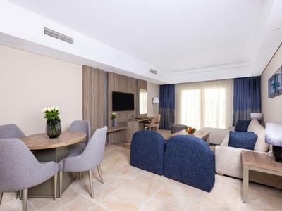 Nowoczesnie urządzony pokój hotelowy z częścią wypoczynkową, stołem jadalnym i dużymi oknami
