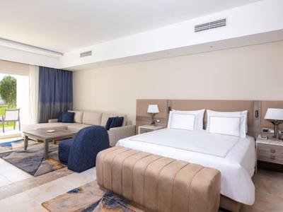 Elegancki pokój hotelowy z dużym łóżkiem, częścią wypoczynkową i widokiem na taras z zielenią.