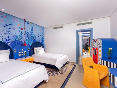Nowoczesny pokój hotelowy z dwoma łóżkami, kolorową ścianą i wygodnymi meblami.