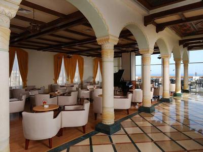 Offener Hotel-Lounge-Bereich mit weißen Sesseln und großen Bögen, Blick aufs Meer im Hintergrund.