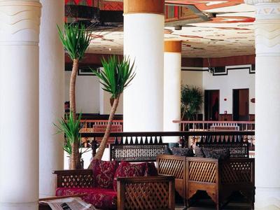 Eleganter Hotel-Loungebereich mit weißen Säulen, dunklen Holzmöbeln und Pflanzen.