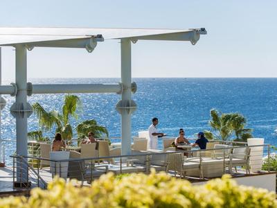 Moderne Terrasse mit Sitzgelegenheiten und Meerblick, Palmen und blauer Himmel im Hintergrund.