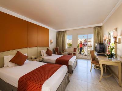 Helle Hotelzimmer mit zwei Einzelbetten, Schreibtisch und Balkon mit Meerblick.
