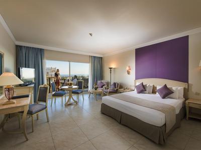 Helles Hotelzimmer mit großem Bett, Schreibtisch, Stühlen und Balkon mit Blick aufs Meer.