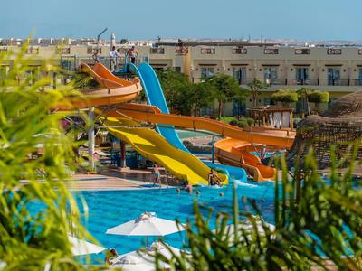 Wasserpark mit bunten Wasserrutschen und blauem Pool, umgeben von grünen Pflanzen und Gebäuden.