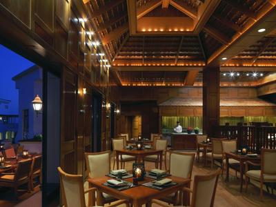 Przytulna restauracja hotelowa z drewnianymi belkami, zastawionymi stołami i klimatycznym oświetleniem o zmierzchu.