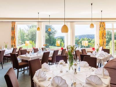 Eleganter Speisesaal mit eingedeckten Tischen und großer Fensterfront mit Blick auf Garten und Berge.