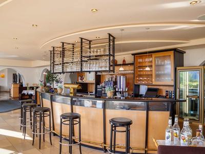 Moderner Barbereich mit hellem Holz, schwarzen Barhockern und Glasregalen für Flaschen und Gläser.