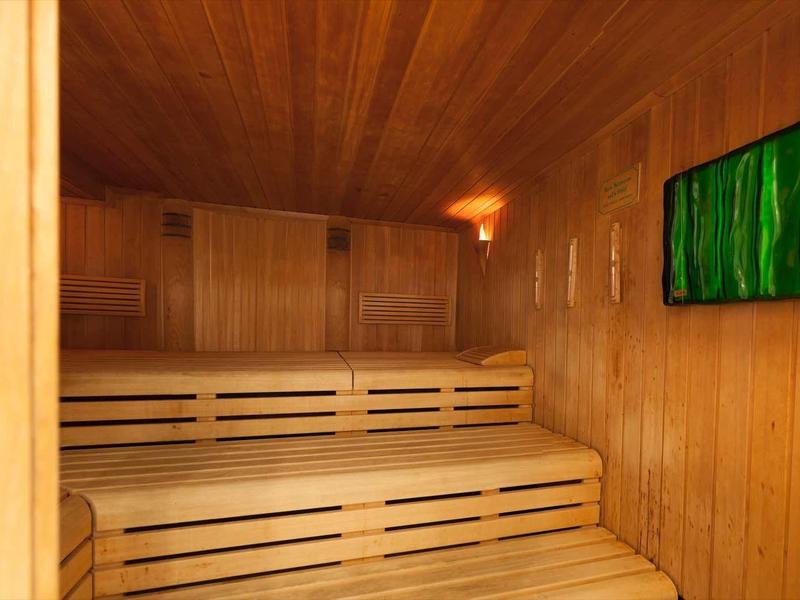 Sauna mit Holzverkleidung, zweistufigen Sitzbänken und grünem Leuchtbild an der Wand.