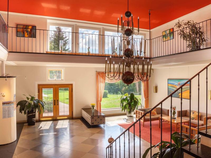 Großes Wohnzimmer mit roten Wänden, hohen Fenstern, Treppe und antikem Kronleuchter.