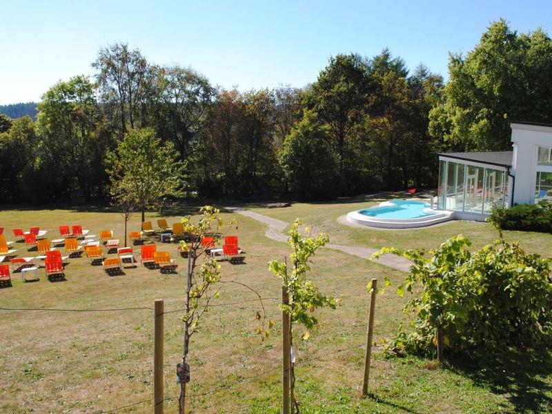 Grünes Gelände mit Bäumen, vielen bunten Sitzplätzen und einem kleinen Pool neben einem Gebäude.