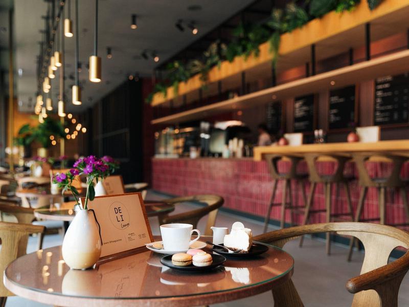 Gemütliches Café mit runden Holztischen, Lederstühlen und einer langen Bar im Hintergrund.