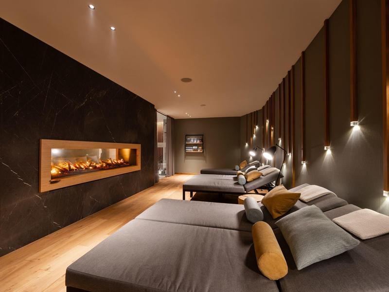 Modern gestalteter Ruheraum mit dimmbarer Beleuchtung, mehreren Liegen und eingebautem Kamin.