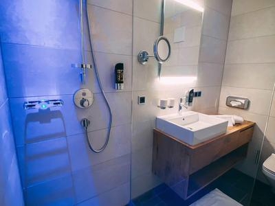 Modernes Badezimmer mit begehbarer Dusche, weißem Waschbecken und Spiegel mit Beleuchtung.