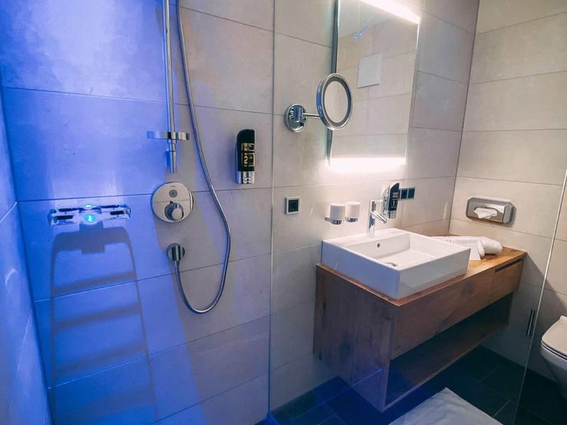 Modernes Badezimmer mit Duschbereich, Waschbecken, beleuchtetem Spiegel und weißen Fliesen.