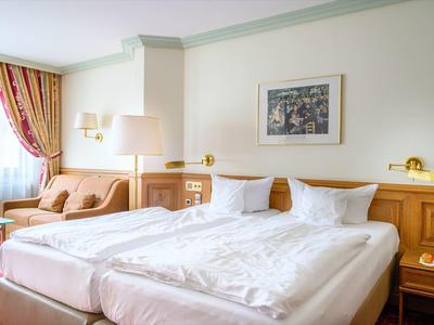 Hotelzimmer mit zwei Einzelbetten, Sofa, rotem Teppich und hellen Holzmöbeln.