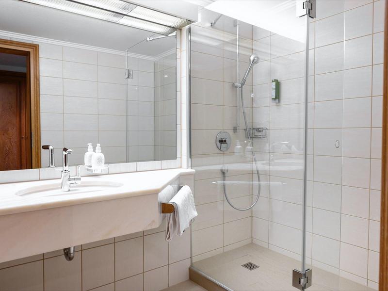 Helles Bad mit großer Spiegelwand, Dusche mit Glasabtrennung und Holztür.