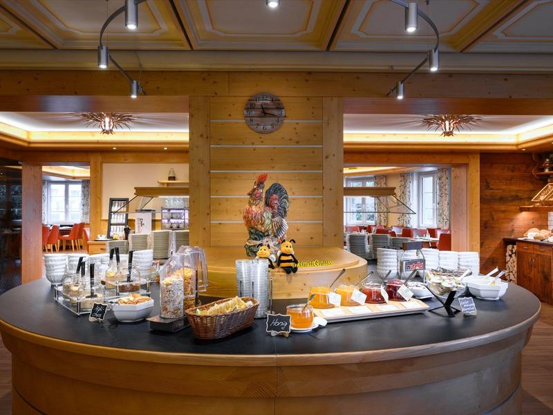 Gemütlicher Frühstücksraum mit Holzwänden, langer Theke und vielfältigem Buffetangebot.