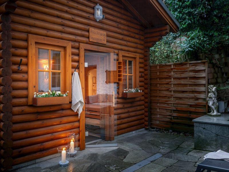 Holzblockhaus mit Fenster, Tür, Kerzen und Schirm auf Steinboden im Garten bei Abenddämmerung.