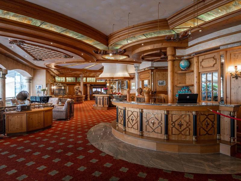 Großer, eleganter Hotel-Lobby mit hölzernem Tresen, roten Teppichen und gemütlichen Sitzecken.